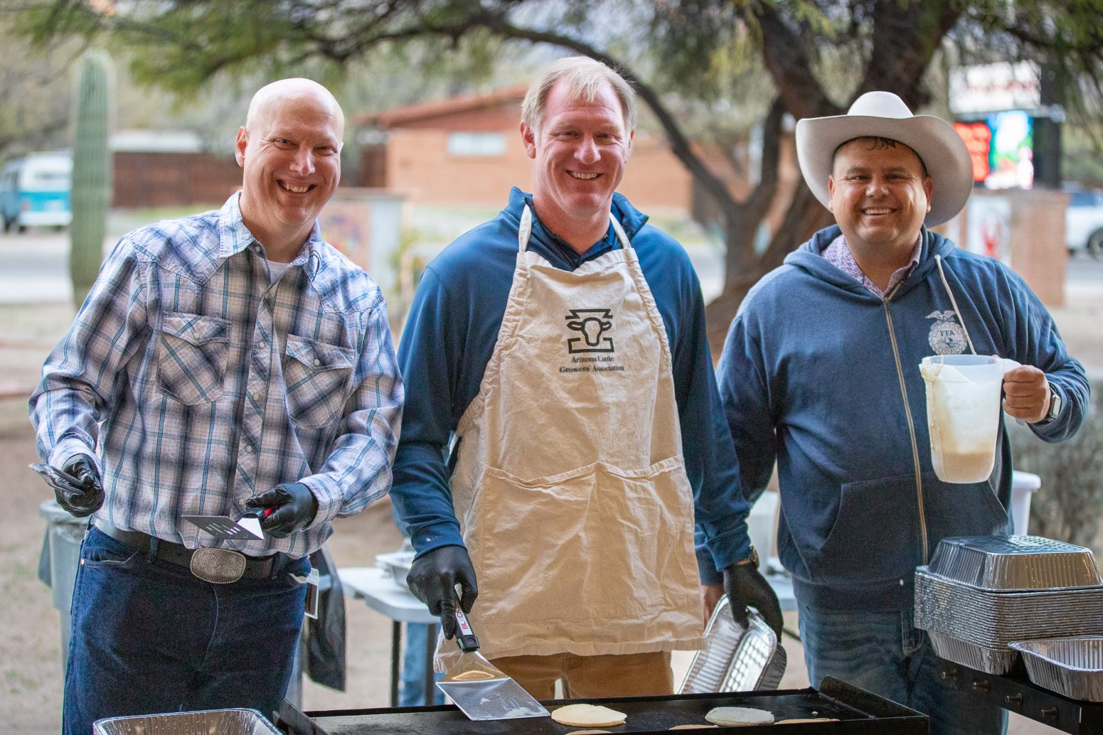 Three men smile as they prepare breakfast for families