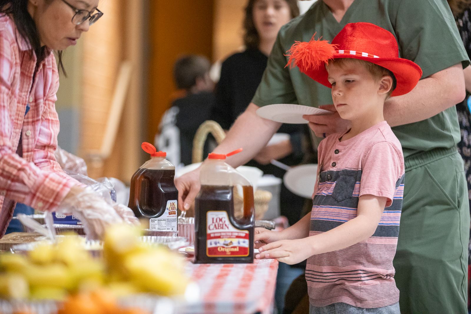 A staff member serves up pancakes to a little boy in a red cowboy hat