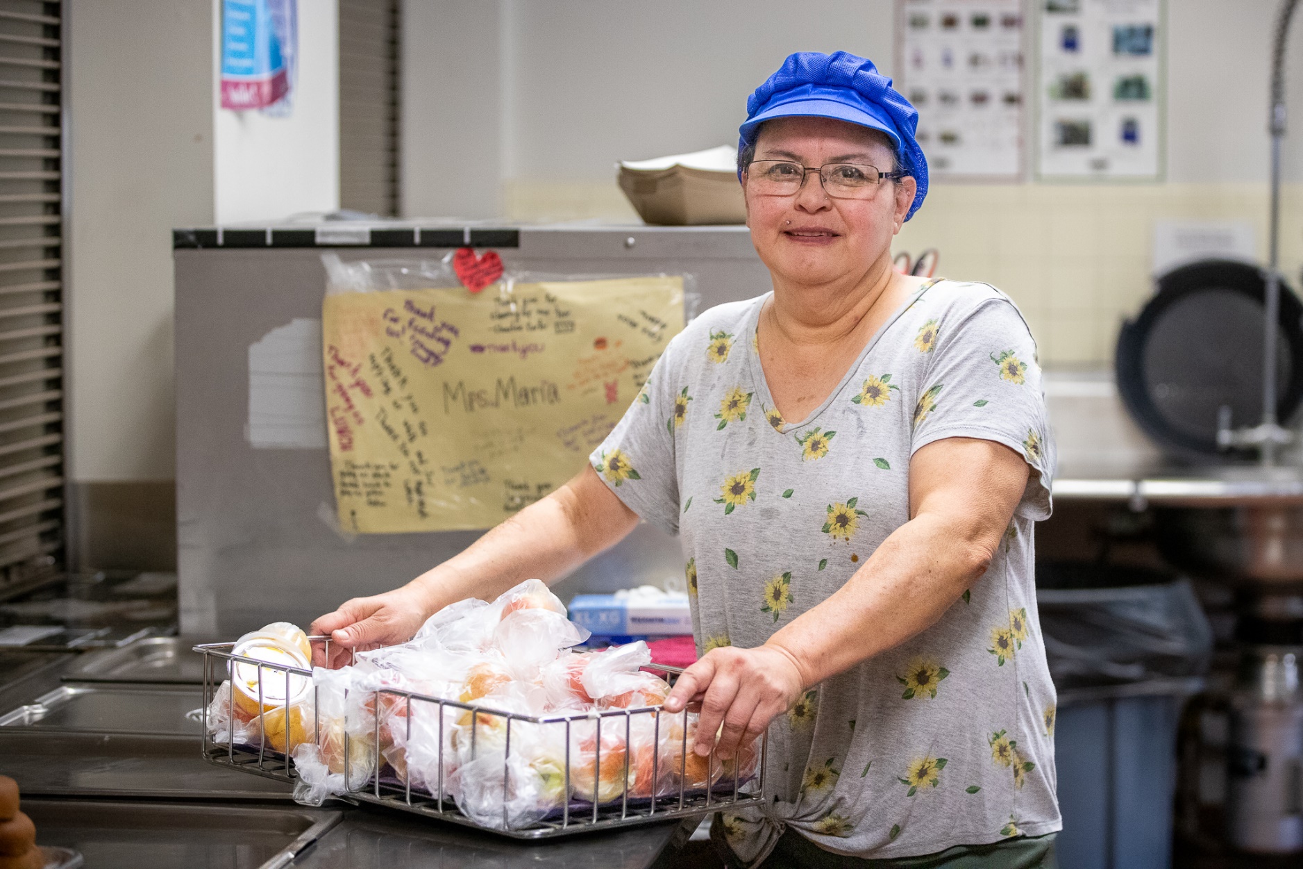 A woman in a blue cap holds a basket of apples