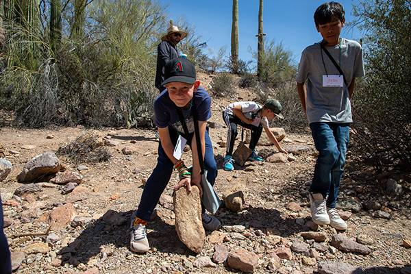 A boy rolls a rock through the wash